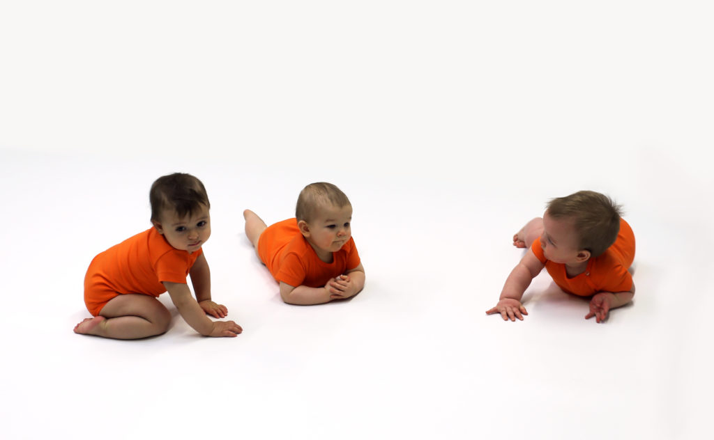 Kuvassa on kolme oransseihin paitoihin puettua vauvaa.