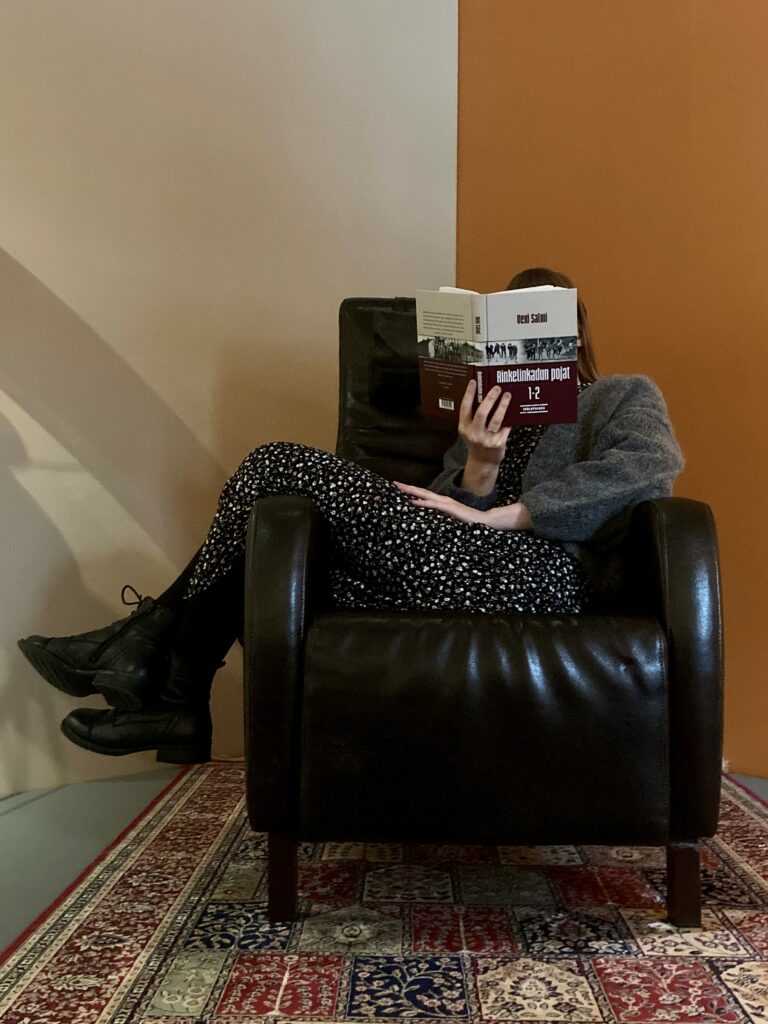 Nainen istuu rennosti nojatuolissa lukemassa kirjaa.