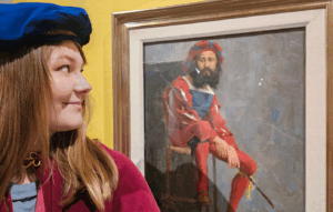 Kuvassa rooliasuun pukeutunut opas katsoo maalausta